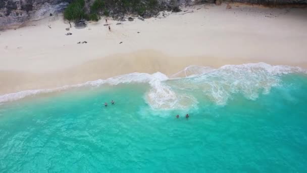 Atemberaubende Luftaufnahme des Kelingking-Strandes mit malerischen Meereswellen, Silhouetten von Menschen und Mantas, die unter den Füßen der Reisenden im Meer treiben — Stockvideo