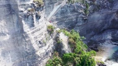 Turistler, Endonezya 'nın Bali adasındaki Nusa Penida Adası' ndaki Diamond Beach 'teki bir kayada kesilen dik bir merdivenden tırmanıp iniyorlar. Hava görüntüsü 4K