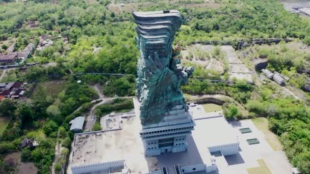 Аэросъемка вокруг статуи Гаруды Висну Кенканы на Бали, Индонезия. Знаменитая религиозная статуя с жилыми кварталами на заднем плане — стоковое видео