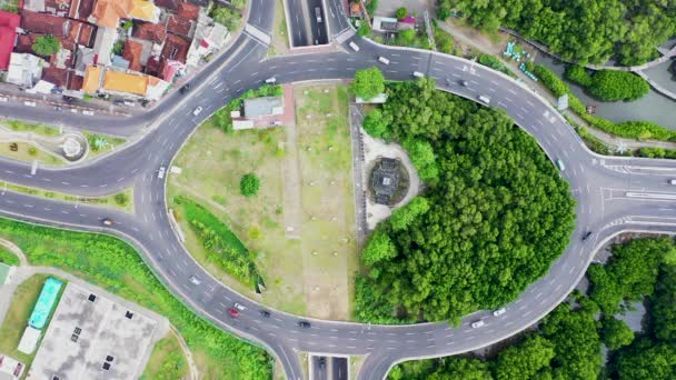 Vue aérienne du haut vers le bas d'un rond-point vert et suivant les voitures en mouvement. Au rond-point avec passage souterrain. Circuit achalandé à l'aéroport international de Bali — Video