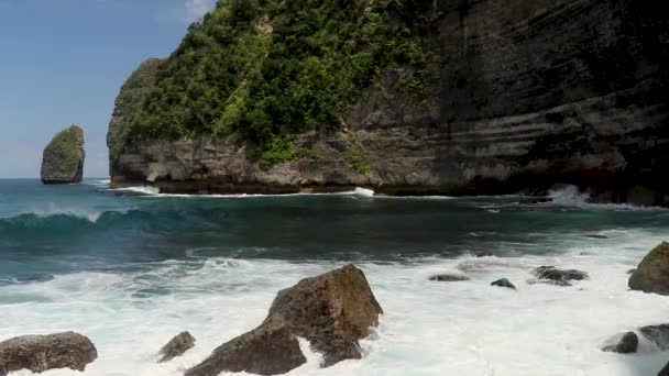 Sinematik azure, biru, hijau, gelombang pirus menerjang pemandangan gunung berapi tebing laut dan batu tajam. Pantai berbatu Pantai Tembeling di pulau Nusa Penida. Gelombang besar menerjang di pantai berbatu — Stok Video