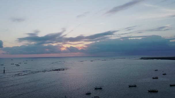 Glänsande gyllene solnedgång med gul himmel och solstrålar genom grå moln reflekterar på lugn lagun med förankrade båtar på Bali — Stockvideo