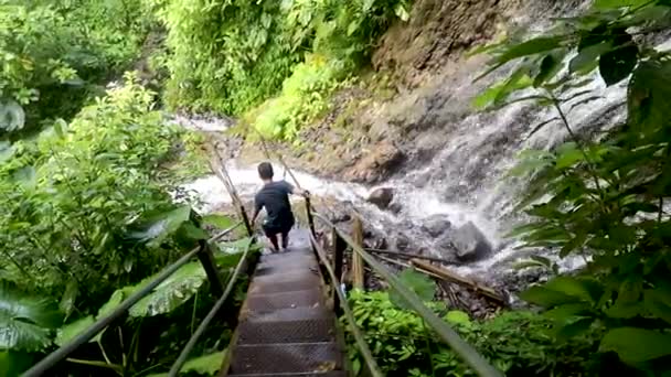 Un homme descend les escaliers en fer jusqu'à une cascade dans la forêt tropicale. Un voyage aventureux et stimulant à travers la forêt tropicale. Un touriste descend dans un canyon dans la jungle — Video