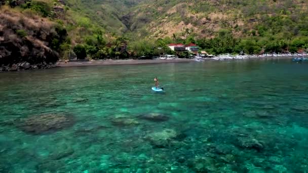 Aerial view of young girl stand up paddling on vacation. Tracking shot of a young woman SUP boarding. Woman on stand up paddle board at blue sea — Stock Video