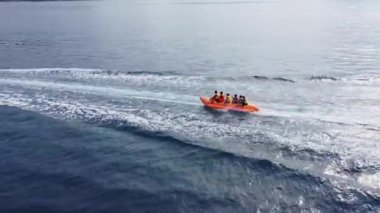 Mutlu insanlar şişirilebilir su aracı muzuna binerler. Deniz eğlencesi, muz teknesi, hava manzarası. Tropik bir adada su sporları ve eğlence. Yaz ve seyahat tatil konsepti