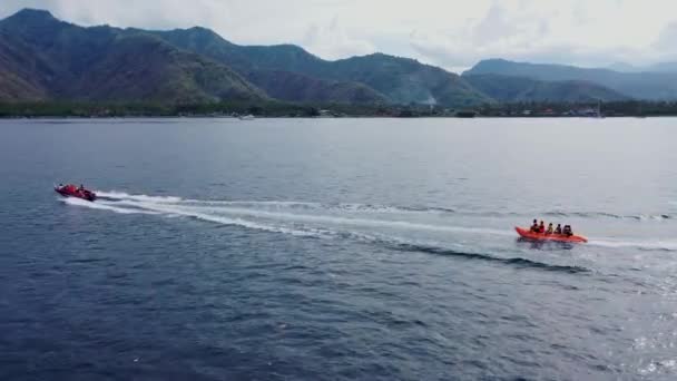Banana boat aventura cena aérea vídeo. Drone aéreo vista lateral rastreamento banana barco passando em alta velocidade no mar azul azure. Barco de borracha laranja — Vídeo de Stock