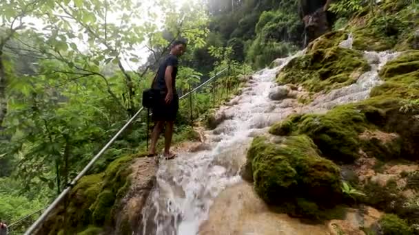 Senderismo hombre trekking en la selva tropical. vista de un joven excursionista caminando por la densa naturaleza de la selva tropical en Indonesia con una hermosa cascada — Vídeos de Stock