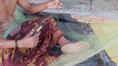 Yaşlı bir balıkçı, Essaouira, Fas 'taki limanda iğne ve iplikle ticari bir balık ağını onarıyor. El işi.