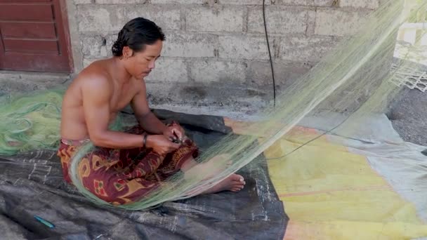 Vissers repareren netten ter voorbereiding op de visserij in zee. Balinese man naait een visval in Bali, Indonesië — Stockvideo