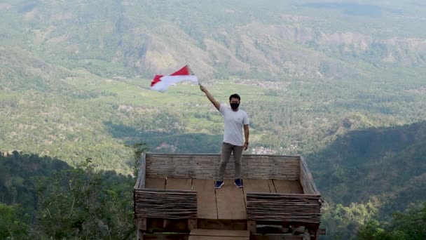 Porträtt av mannen på toppen av kullen på morgonen stigande indonesiska flaggan firar självständighetsdagen — Stockvideo