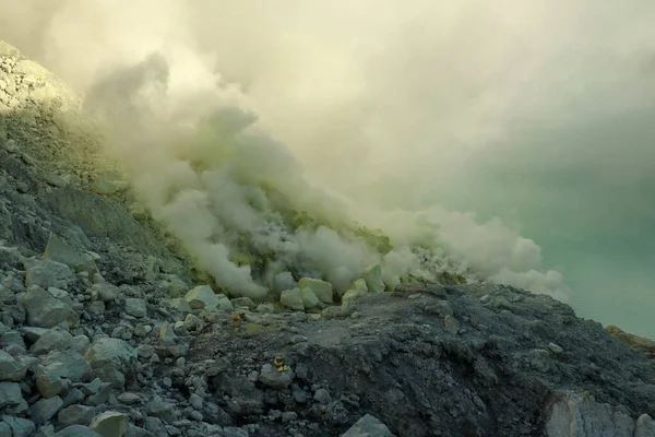 Lago del cráter volcánico Kawah Ijen y humo tóxico de azufre, los trabajadores extraen azufre de esta zona ahumada y llevan una cesta de 80-90 kg llena de azufre en el hombro y descargan las canastas a 3,5 km de distancia. —  Fotos de Stock