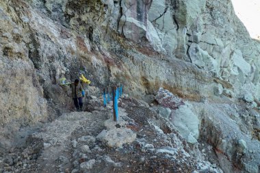 Ijen Volcano, Banyuwangi Regency, Java, Indonesia, 2 June 2021. Indonesian sulfur miner is carrying his 90-kg-load of sulfur from the floor of the volcano to the valley where he is getting paid