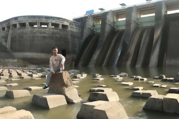 Een jongeman zit op betonnen blokken onder een dam Bendungan Sampean Baru op Java, Indonesië — Stockfoto