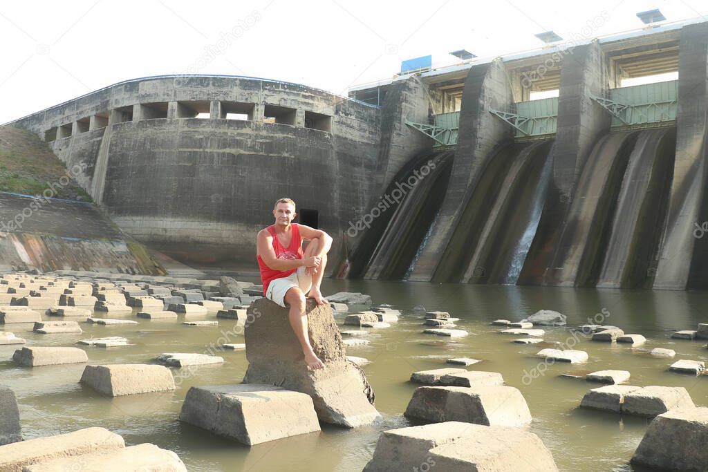A man sits on concrete blocks under a dam. Dam and Waterfall Bendungan Sampean Baru in Bondowoso East Java Indonesia