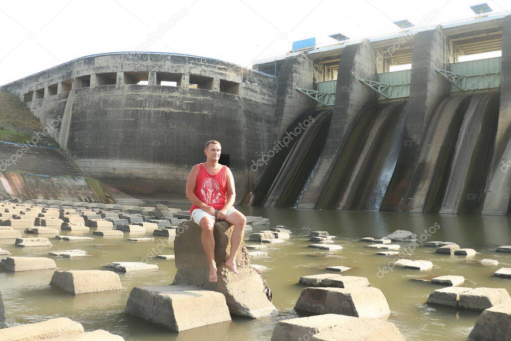 A man sits on concrete blocks under a dam. Dam and Waterfall Bendungan Sampean Baru in Bondowoso East Java Indonesia