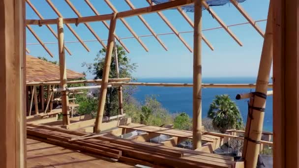 Vol de drone A l'intérieur d'une maison en bois en construction. Photo détaillée d'un toit en bois chevauchant la construction. Vue sur la mer et la côte tropicale — Video