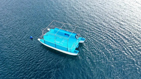 Drone aéreo de cima para baixo foto de catamarã pequeno ancorado no mar azul profundo. Um pequeno catamarã azul no mar aberto — Fotografia de Stock