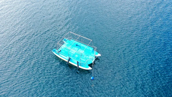 Drone aéreo de cima para baixo foto de catamarã pequeno ancorado no mar azul profundo. Um pequeno catamarã azul no mar aberto — Fotografia de Stock