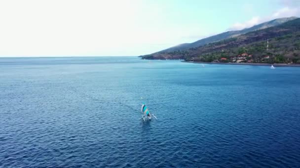 Vista aérea do barco de pesca tradicional chamado jukung perto da praia de areia preta. Barco de pesca branco com uma vela branca — Vídeo de Stock