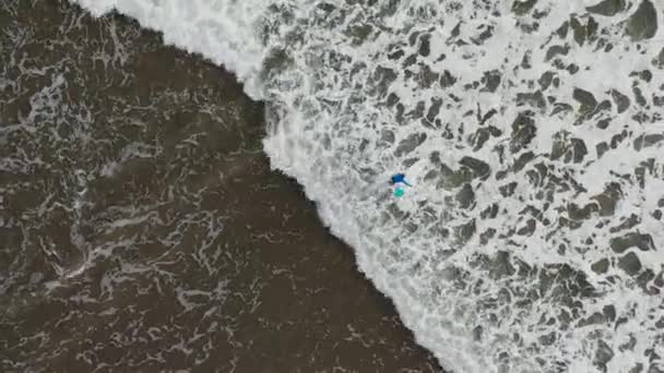 Los jóvenes surfistas caminan en las olas en aguas poco profundas. Un niño camina en olas oceánicas. Moderno estilo de vida activo. Campamento de deportes acuáticos. Extremo en las vacaciones de verano. Imágenes aéreas de aviones no tripulados — Vídeo de stock