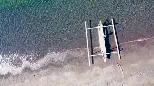 Nagranie z góry na dół tradycyjnej łodzi rybackiej na czarnej wulkanicznej plaży z piaskiem i płytkiej turkusowej wody — Wideo stockowe