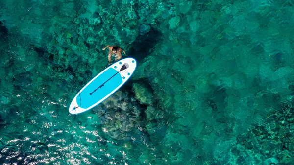 Aereo drone top down foto di donna in forma si rilassa donna nel mare accanto a una scheda SUP. Ragazza in mare con Stand Up Paddle board in tropicale esotico turchese mare limpido — Foto Stock
