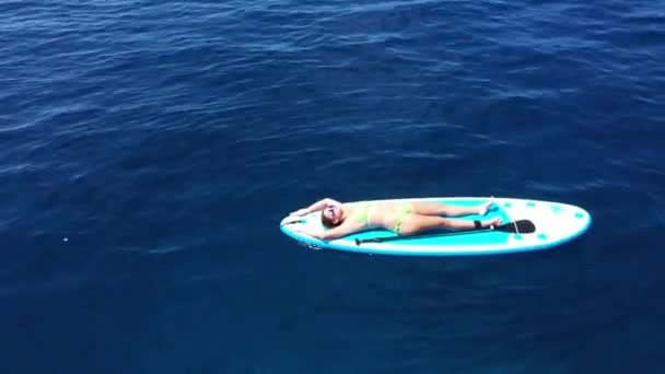 Young woman floating On Sup Board With Paddle On Water. Drone aerial shot of woman sunbathing on surfboard.Aerial view. Extreme Summer Water Sports. Healthy Lifestyle. Surfing. 4K — Stock Video