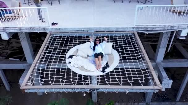 Bali, Indonésia, 1 de setembro de 2021. Jovem bela mulher asiática rindo sentado e acenando com as mãos em uma rede sobre um vale em Montana del Cafe. Adeus, drone selfie. Tiro aéreo. Conceito de viagem — Vídeo de Stock