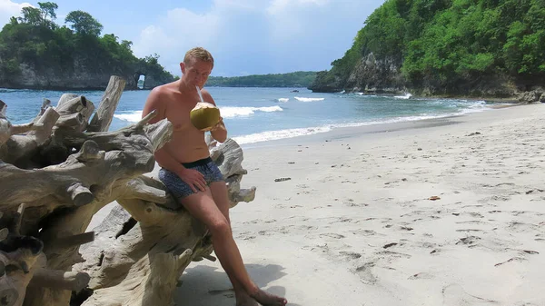 Homme du Moyen Âge appuyé sur un arbre sec mort sur la plage reposant et buvant de la noix de coco verte fraîche. Concept de vacances — Photo