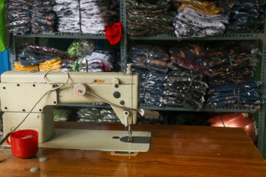 Arka planda kumaş yığınları olan terzi atölyesinde dikiş makinesi..