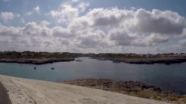 mavi yaz gökyüzü ile mesafede oyma kayalıklar ve eski bir fort ile menorca cala santandria de körfezin doğal bir görünüm