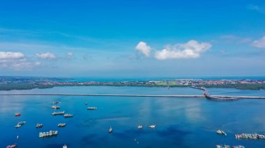 Koyu mavi suyun üzerindeki Tanyung Benoa Yarımadası 'nın ucundaki sahil, iskele, tekne, tatil köyü ve iş yerleri. Yeşil yapraklar ve kırmızı çatılar..