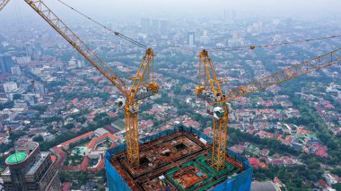 İnşaat halindeki bir gökdelenin çatısındaki vinçler. Bulutlu bir sabahta inşaat sahası.