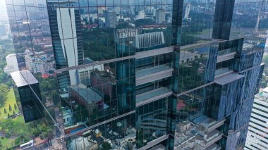 Drone vertical flight among the modern futuristic skyscrapers in Jakarta City business centre, sunset reflection in shiny glass facade.