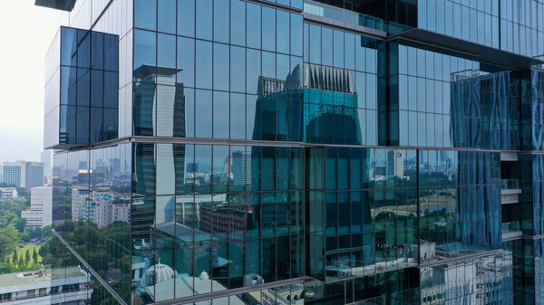 Drone vertical flight among the modern futuristic skyscrapers in Jakarta City business centre, sunset reflection in shiny glass facade.