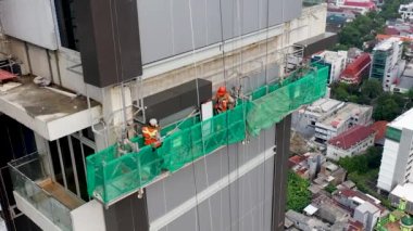 Dış görünüş yalıtımı. İnşaatçılar evi izole eder. Gökdelendeki askıya alınmış platformda inşaat işçileri. Profesyonel işçiler. İnşaat alanı. Konut kompleksinin geliştirilmesi.