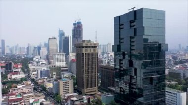 Drone vertical flight among the modern futuristic skyscrapers in Jakarta City business centre, sunset reflection in shiny glass facade.