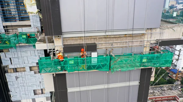 Suspended platform, construction cradle hanging on building. Installation and repair work. Building facades construction works. Glass facade of high-rise building under construction, finishing works.