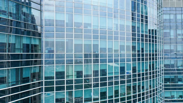 The glass facade of a skyscraper with a mirror reflection of sky windows.