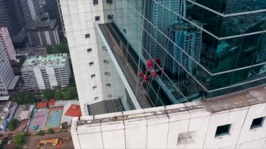 Dört Cam Temizleyicisi bir gökdelenin kenarında. Turuncu un kaplamalı çamaşır makineleri cam perdenin kenarından sarkan cam pencereleri temizliyor.