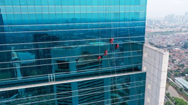 Endüstriyel tırmanışçılar modern gökdelenlerin camlarını silerler. Mavi tonlu resim.
