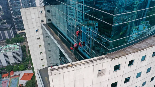 Four Window Washers Cleaning on the side of a skyscraper. Washers in orange flouro tops hang off side of glass curtain building cleaning exterior glass windows.