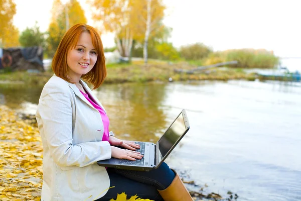 Aantrekkelijk meisje met laptop over een reservoir in de herfst — Stockfoto