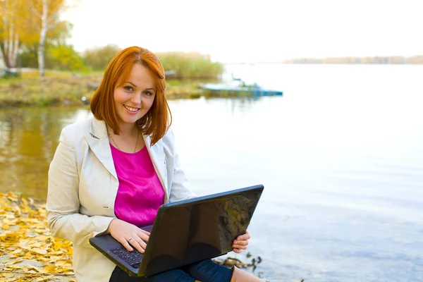 Attraktives Mädchen mit Laptop über einen Stausee im Herbst — Stockfoto