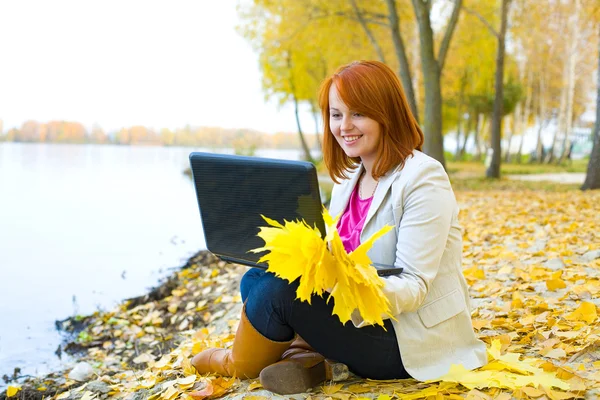 La muchacha atractiva con el portátil sobre el aljibe en otoño — Foto de Stock