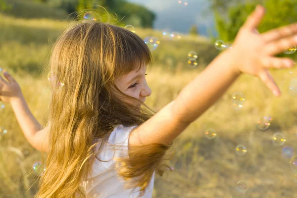 Kleines positives Mädchen fängt Seifenblasen — Stockfoto