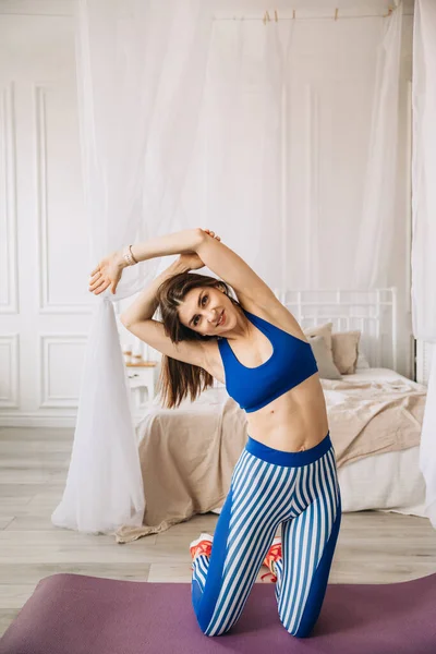 Sportif kız sabah evde, yatağın yanında ısınma egzersizi yapıyor..