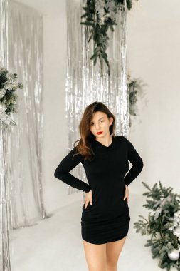 Siyah elbiseli manken beyaz stüdyoda sandalyede poz veriyor.