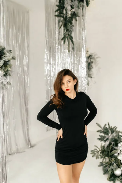 Siyah elbiseli manken beyaz stüdyoda sandalyede poz veriyor.