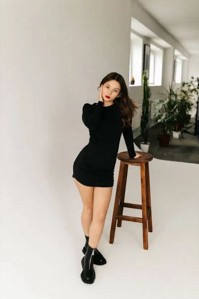 Young girl in a black dress posing with a chair in the studio — Stock Photo, Image